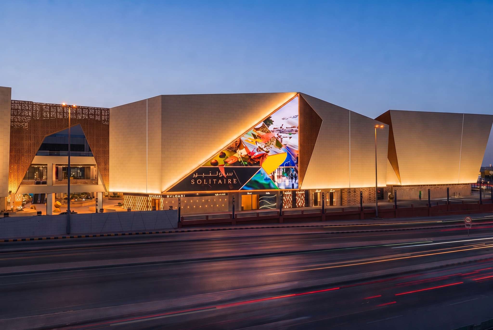 Solitaire Mall in Riyadh at dusk, its stone facade lit, seen from across the road